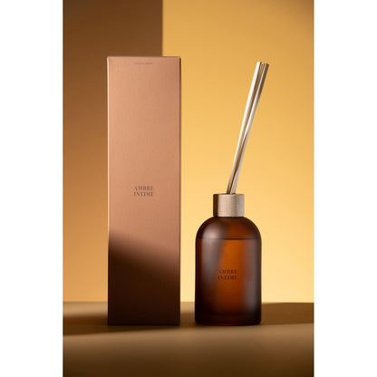 Geurstokjes Accords Essentiels Ambre Intime 550ml van J-Line gestyled tegen een okerkleurige wand met zacht licht